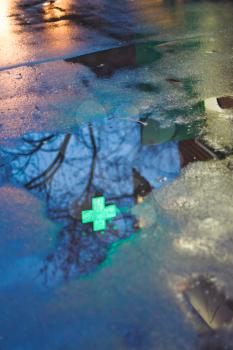 pharmacy cross reflection in rain puddle in dark urban evening