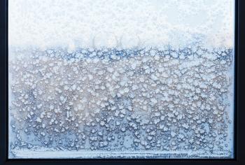 snowflakes and frost pattern on frozen windowpane in cold winter day