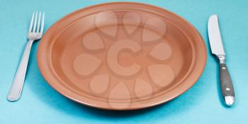 empty brown ceramic plate with fork and knife on green background