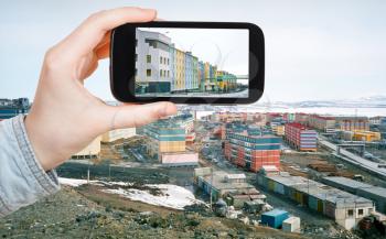 travel concept - tourist taking photo of Anadyr town on mobile gadget in spring, Chukotka, Russia