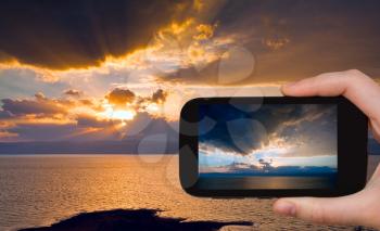 travel concept - tourist taking photo of sundown on Dead Sea on mobile phone, Jordan
