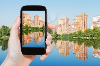 travel concept - tourist taking photo of brick apartment houses along waterfront on mobile gadget
