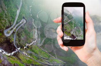 travel concept - tourist taking photo of Trollstigen (Trolls Path) serpentine mountain road in Norway on mobile gadget