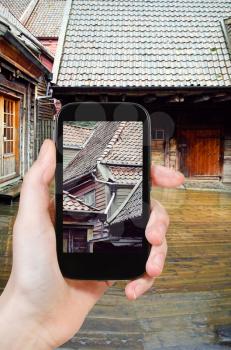 travel concept - tourist taking photo of wooden houses in rain, Bergen, Norway of on mobile gadget