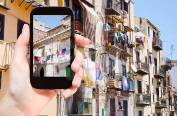travel concept - tourist taking photo of municipal house in Palermo in summer day, Italy on mobile gadget