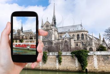 travel concept - tourist taking photo of cathedral Notre Dame de Paris and tourist boat on Seine River on mobile gadget, France