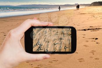 travel concept - tourist taking photo of sand beach on Atlantic coast in Algarve, Portugal on mobile gadget