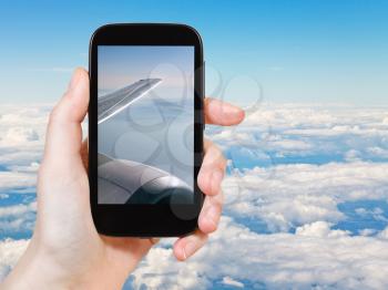 travel concept - tourist taking photo of white clouds under wing of airplane on mobile gadget