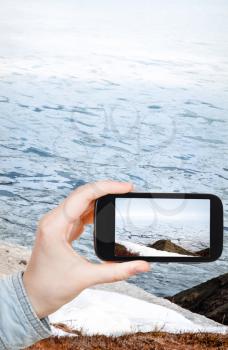 travel concept - tourist taking photo of ice floes on coastline of Bering Sea on mobile gadget