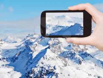 travel concept - tourist taking photo of snow mountains in Alpes Paradiski skiing domain, Les Coches - Montchavin , France on mobile gadget