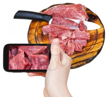 photographing food concept - tourist takes picture of cut raw meat on cutting wooden board on smartphone,