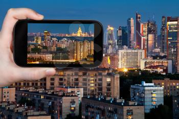 travel concept - tourist takes picture of panorama of Moscow city in blue summer night on smartphone,