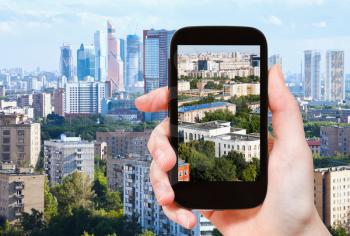 travel concept - tourist takes picture of Moscow City and urban living area in Moscow in summer afternoon on smartphone,