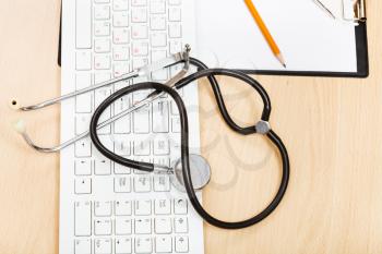 medical still life - stethoscope on white keyboard and blank clipboard
