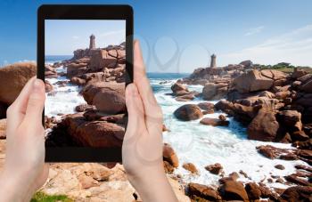 travel concept - tourist takes picture of lighthouse in the rocks on Pink Granite Coast in Brittany, France on tablet pc