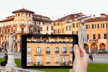 travel concept - tourist takes picture of facade of medieval house on piazza Prato della Valle in Padua in evening on tablet pc, Italy