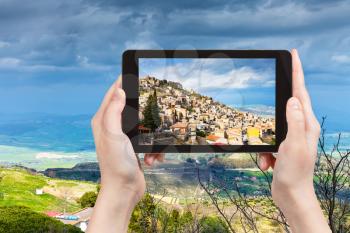 travel concept - tourist takes picture of Aidone town in Sicily in spring, Italy on tablet pc