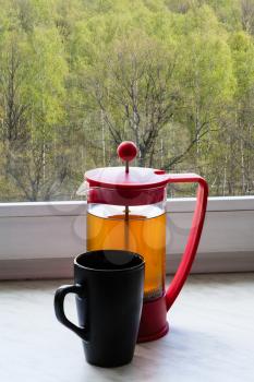 tea kettle and mug on home windowsill and view of spring green forest outdoors