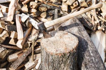 wood cleaver ax in deck for chopping firewood, pile of wood on rustic courtyard