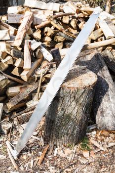 two-handled saw and ax in deck for chopping firewood, pile of wood on rustic courtyard