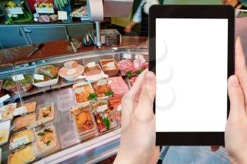 travel concept - tourist photograph meat and delicacies in in small butcher shop in France on tablet pc with cut out screen with blank place for advertising logo