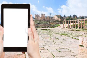 travel concept - tourist photograph colonnade on the Roman Oval Forum in ancient town Jerash in Jordan on tablet pc with cut out screen with blank place for advertising logo