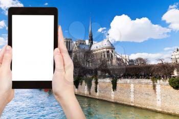 travel concept - tourist photograph cathedral Notre Dame de Paris and Seine River, France in spring on tablet pc with cut out screen with blank place for advertising logo