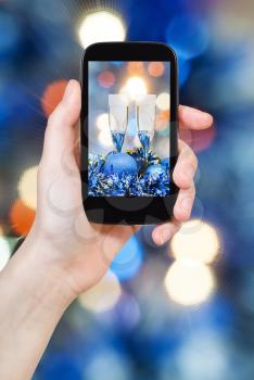 man takes photo of Christmas still life - two glasses of champagne at blue Xmas decorations with pink and blue blurred Christmas lights background