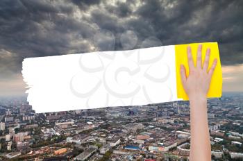 ecology concept - hand deletes storm clouds over city by yellow rag from image and white empty copy space are appearing