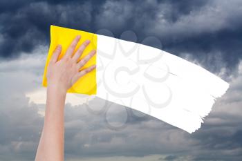 weather concept - hand deletes overcast sky by yellow rag from image and white empty copy space are appearing