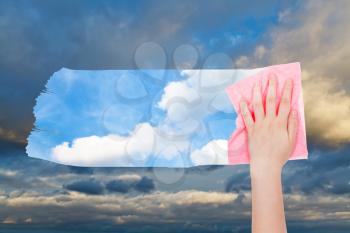 weather concept - hand deletes dark cloudscape by pink cloth from image and blue sky with white clouds are appearing