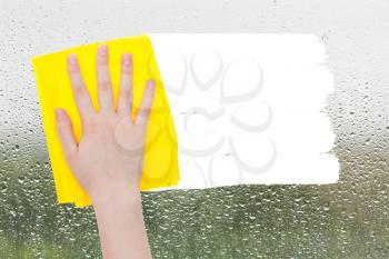 weather concept - hand deletes raindrops on glass by yellow rag from image and white empty copy space are appearing