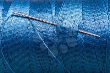 sewing needle in blue thread bobbin close up