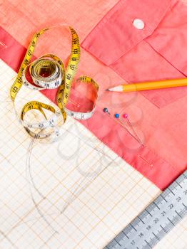 dressmaking still life - above view of cutting table with pattern, measuring tape, pencil, pins, red shirt