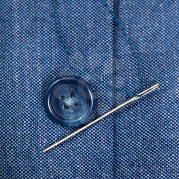 attaching of button to blue silk jacket by needle close up
