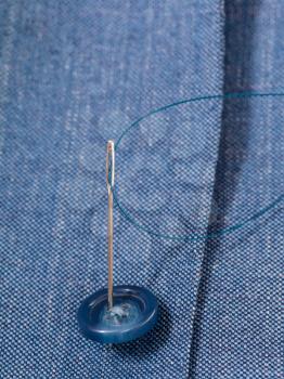 attaching of button to blue silk dress by needle close up