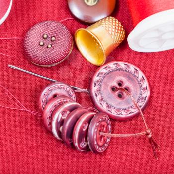 dressmaking still life - top view of bobbins with sewing thread, buttons, thimble, needle on red fabric