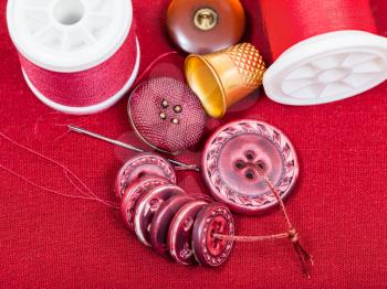 dressmaking still life - top view of bobbins with sewing thread, buttons, thimble, needle on red textile