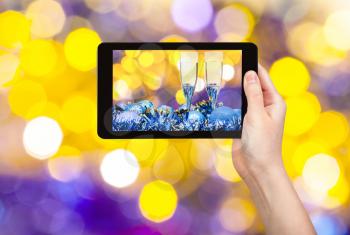 man takes photo of Christmas still life - two glasses of champagne at blue Xmas decorations with yellow and violet blurred Christmas lights bokeh background