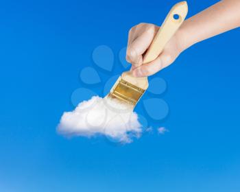 weather concept - hand with paintbrush paints lonely white little cloud in the summer blue sky
