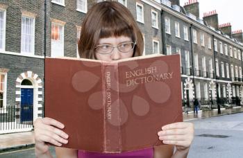 girl with spectacles reads English Dictionary book and typical London houses on background