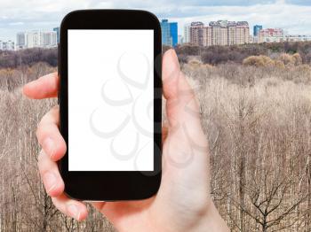 travel concept - hand holds smartphone with cut out screen and bare trees in spring forest on background