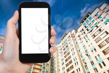 travel concept - hand holds smartphone with cut out screen and new apartment houses on background