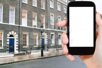 travel concept - hand holds smartphone with cut out screen and London apartment house on background