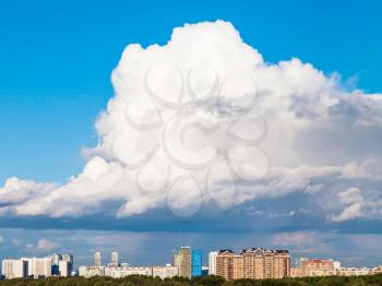 large low white cloud in blue sky over town in summer day