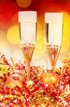 Christmas still life - two glasses of sparkling wine at golden and orange Xmas decorations with yellow and red blurred Christmas lights bokeh background