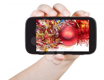 hand holds smartphone with Christmas decorations on screen isolated on white background