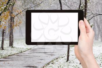 season concept - hand holds tablet pc with cut out screen and first snowfall in urban park on background