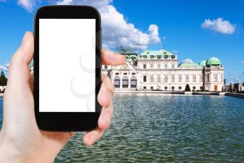 travel concept - tourist takes picture of Upper Belvedere Palace in Vienna on smartphone with cut out screen with blank place for advertising logo