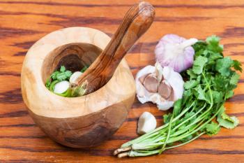 cooking seasonings - wooden mortar with cilantro grass and garlic on table